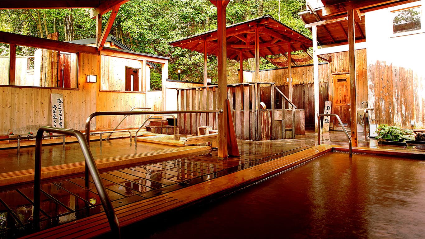 Large outdoor kinsen iron-spring rotenburo with golden-brown water under a red-pillared wooden pavilion at Ginsuiso Choraku