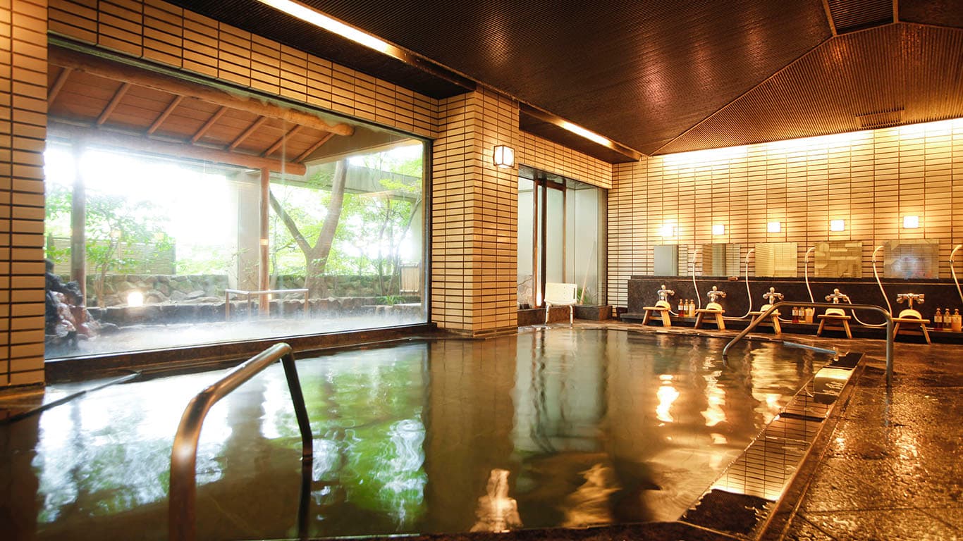 Spacious indoor ginsen public bath with clear mineral water and a garden-view picture window at Ginsuiso Choraku