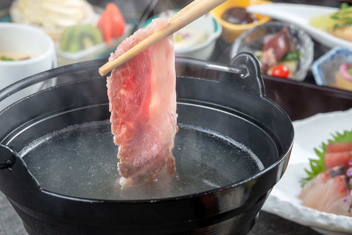 Slice of marbled wagyu beef lifted with chopsticks over a steaming shabu-shabu pot