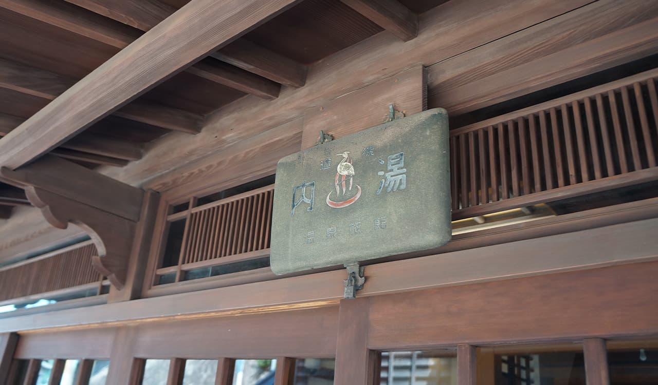Carved stone 'uchiyu' hot-spring plaque hanging under the wooden eaves at Tokiwaso, Dogo Onsen
