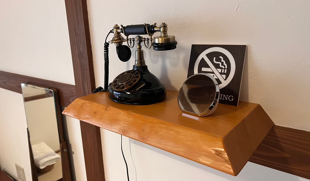 Antique brass rotary telephone displayed on a cedar shelf in a guest room at Tokiwaso, Dogo Onsen