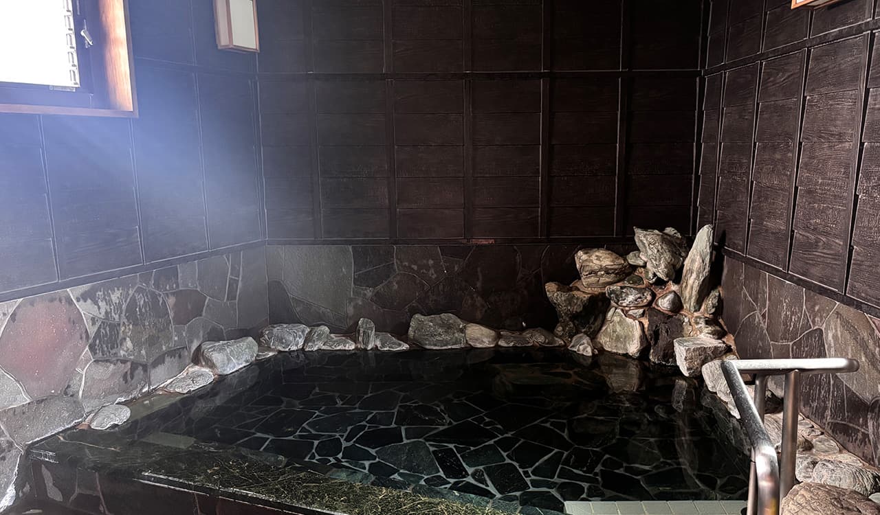 Indoor stone hot-spring bath with rising steam and natural rockwork at Tokiwaso ryokan, Dogo Onsen