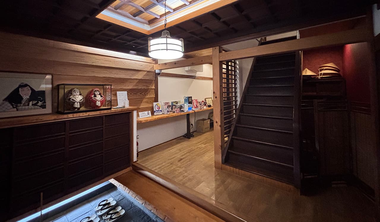 Wooden lobby and entrance hall with staircase, paper lantern and slatted ceiling at Tokiwaso ryokan, Dogo Onsen