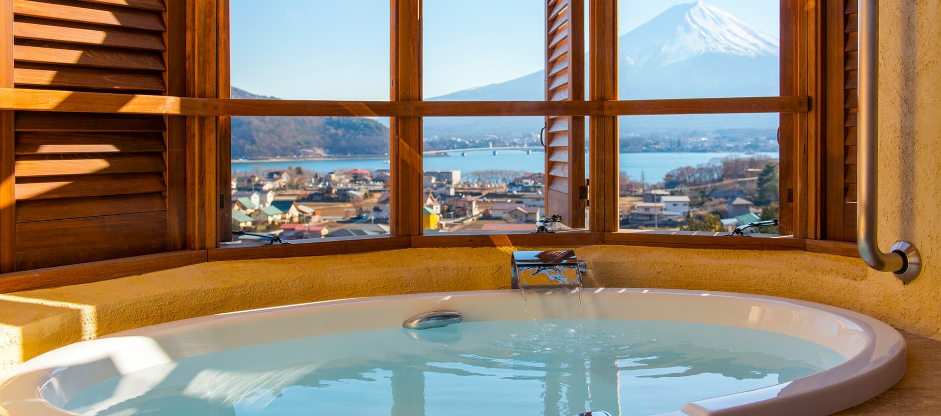 In-room circular hot-spring bath at La Vista Fuji Kawaguchiko set beneath wood-framed windows facing Mt Fuji and Lake Kawaguchiko