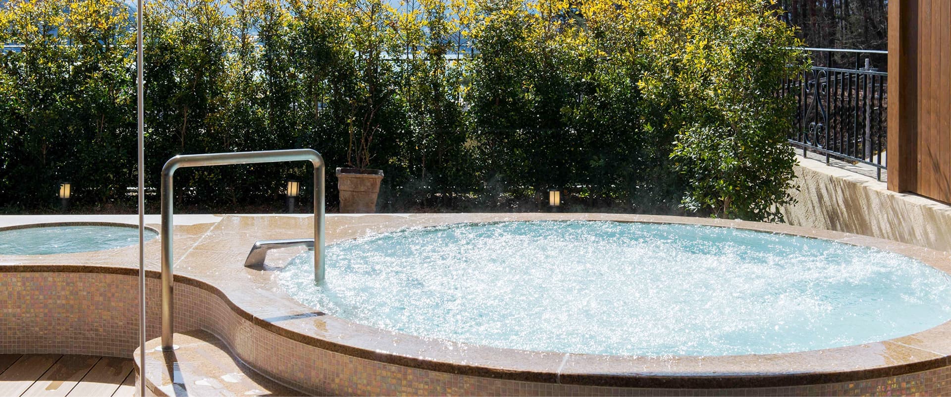 Outdoor bubbling onsen tub at La Vista Fuji Kawaguchiko bordered by green hedges and a wood deck
