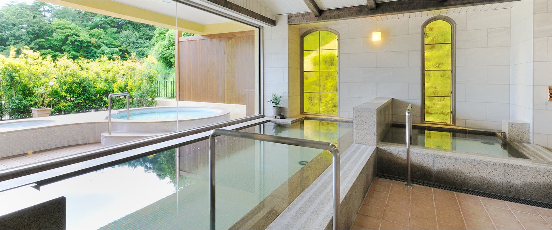 Indoor hot-spring bath (uchiyu) at La Vista Fuji Kawaguchiko with stone tubs, arched stained-glass windows and an adjoining garden bath
