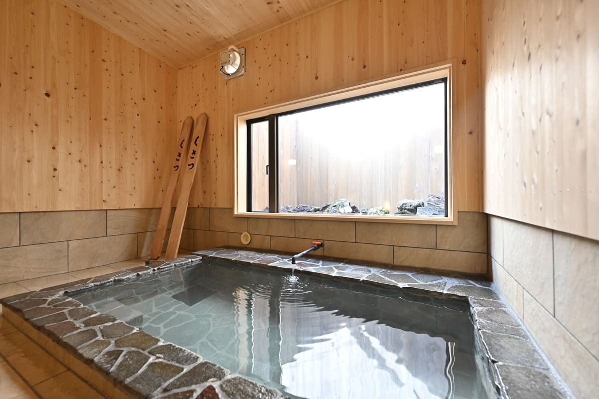Indoor private hot spring bath of stone and cedar wood with a garden-view window