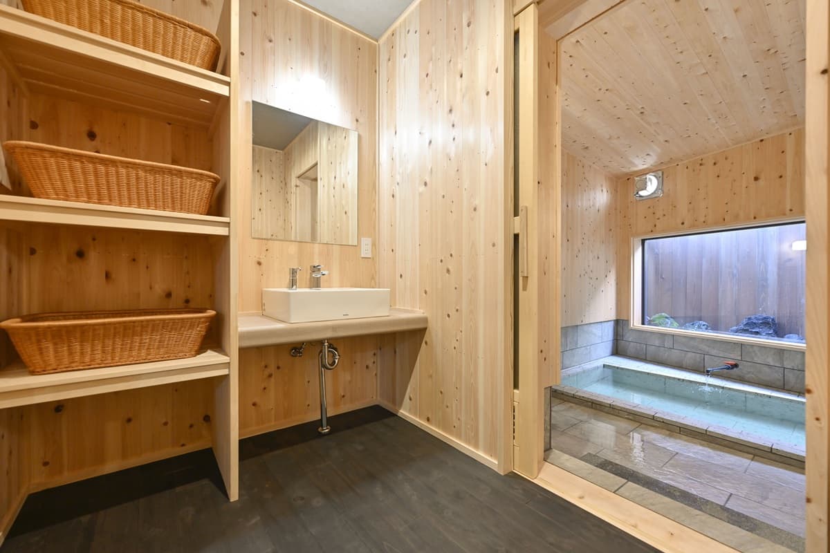 Cedar-lined bath dressing area with vessel sink, woven baskets and stone soaking tub beyond