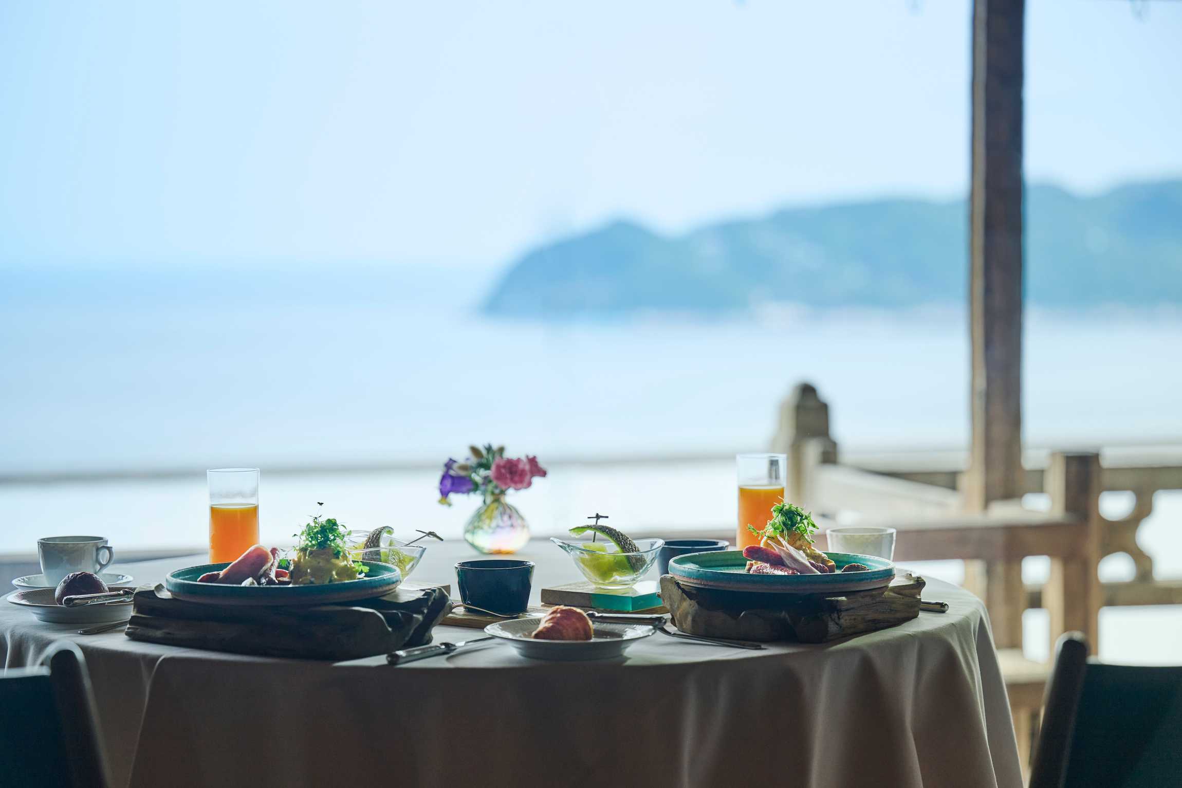 Breakfast set on a draped table at the Hiramatsu Atami with juices, fruit and an open ocean view to Sagami Bay