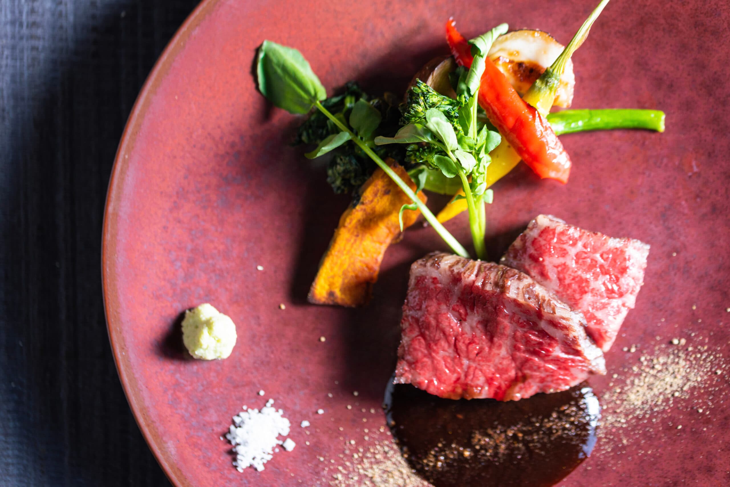 Plated Tajima wagyu beef kaiseki course with grilled vegetables on a deep red ceramic plate at Gosho Bessho