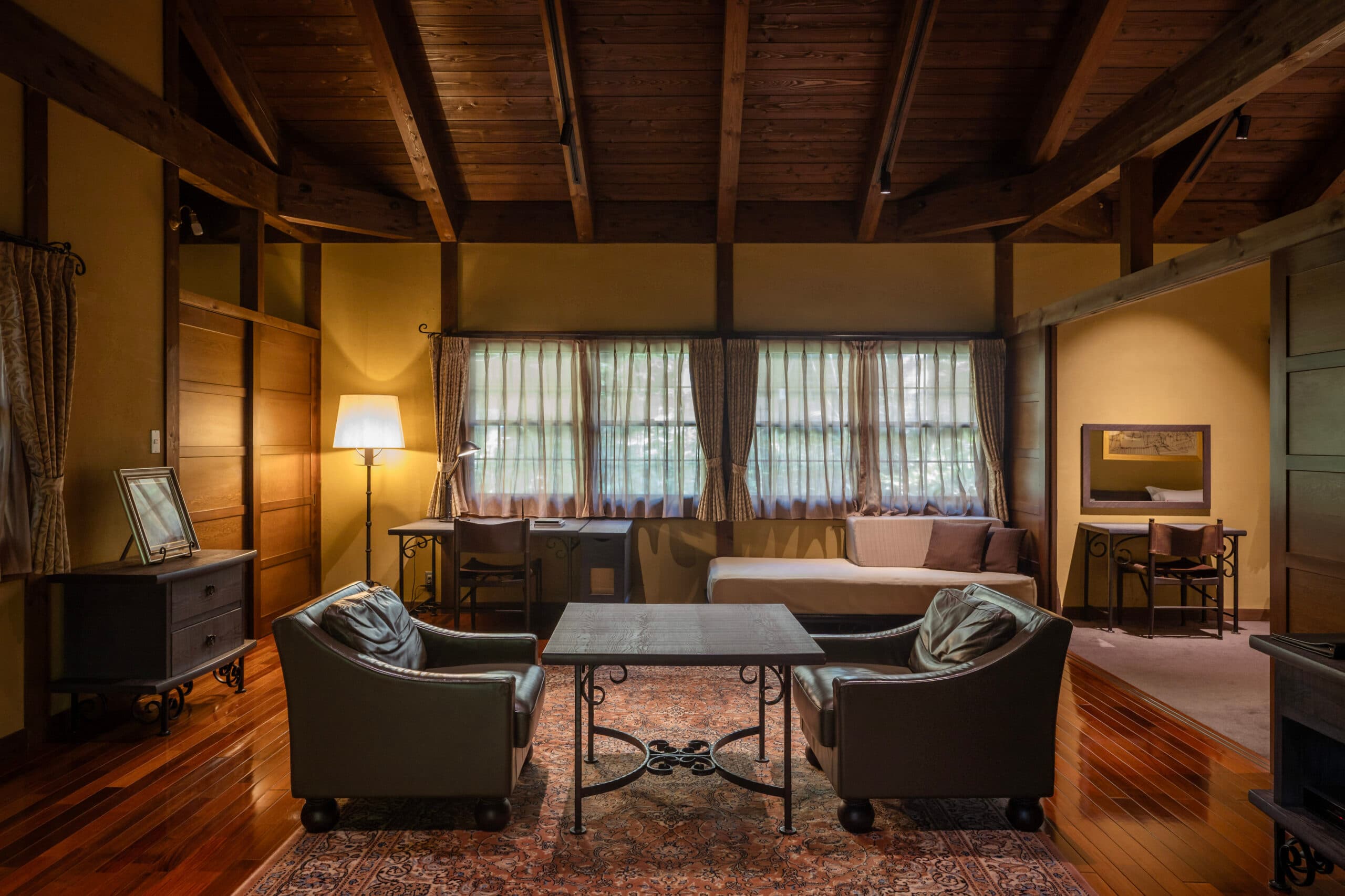Antique-furnished villa living lounge with sofas and timber ceiling beams opening to garden windows at Gosho Bessho