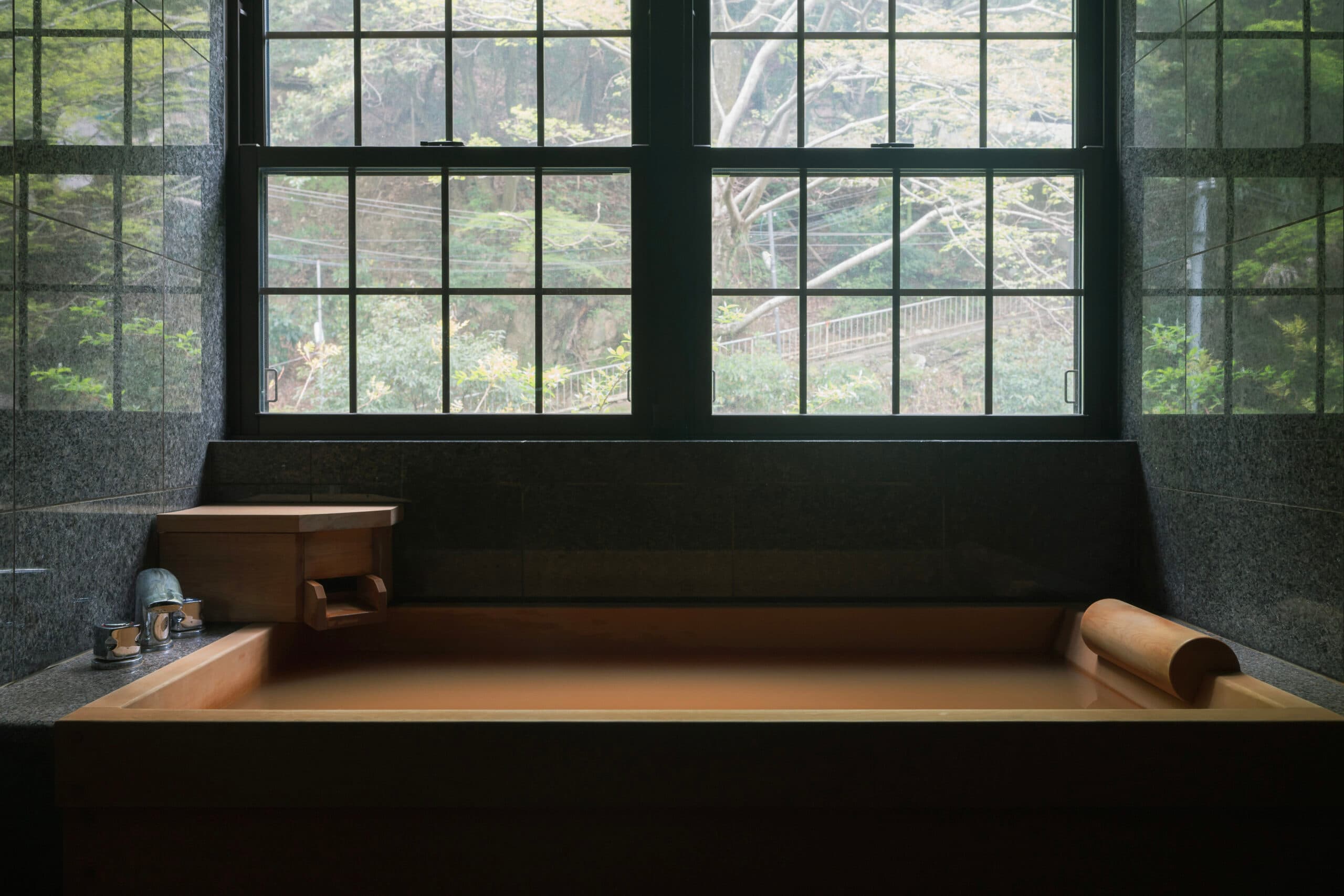 In-villa hinoki cypress soaking bath at Gosho Bessho framed by tall lattice windows overlooking the forest