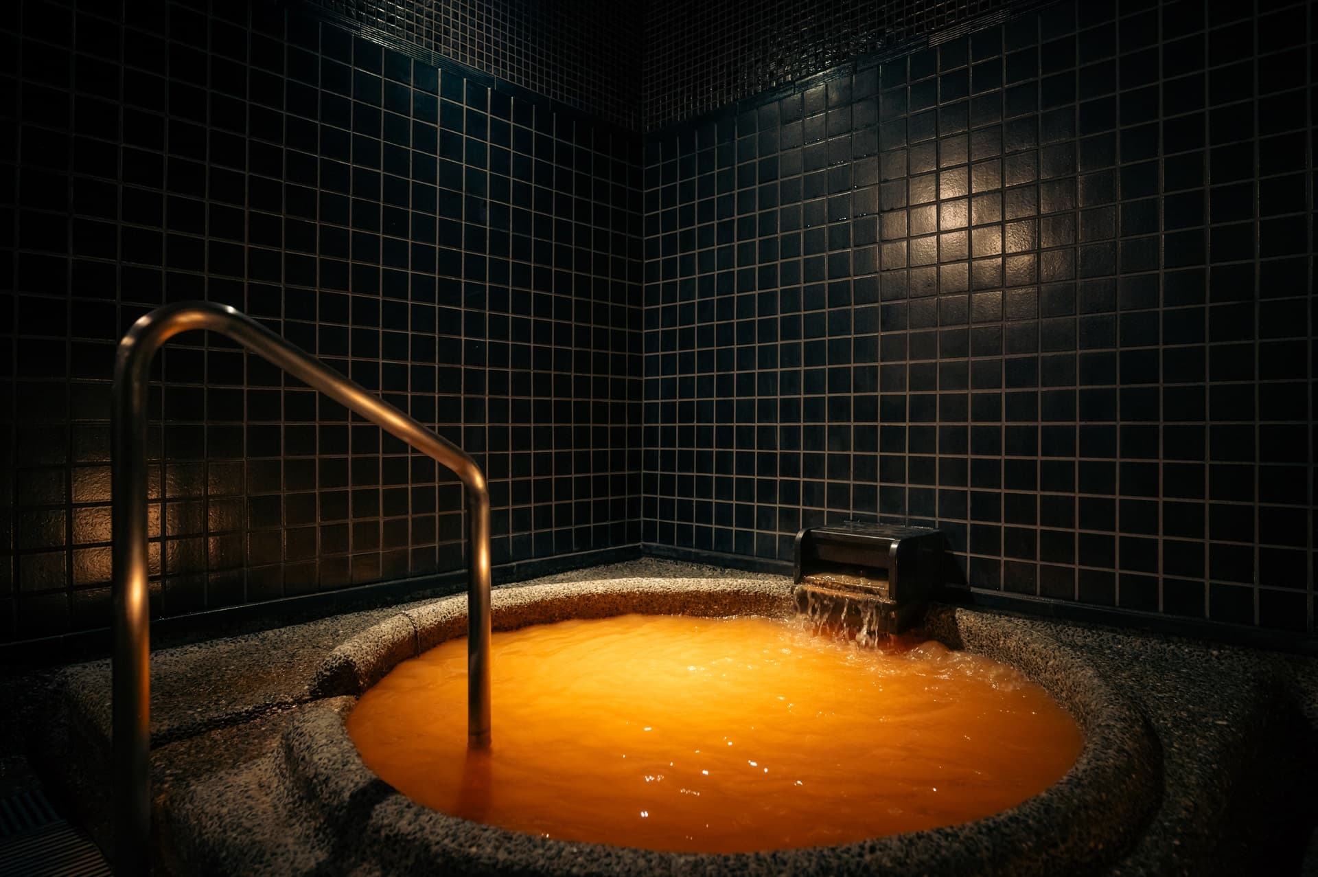 Reddish-brown kinsen gold-spring water flowing into a stone bath against dark tiles at Hotel Hanakoyado, Arima Onsen