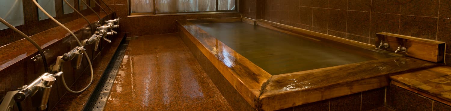 Indoor onsen bath with a wood-edged stone tub and tiled washing area at Hida Takayama Hodakaso Yamano Iori