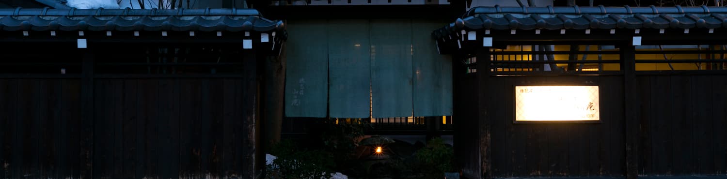 Hida Takayama Hodakaso Yamano Iori dark-timber entrance with indigo noren curtain and lit signboard at dusk in old-town Takayama