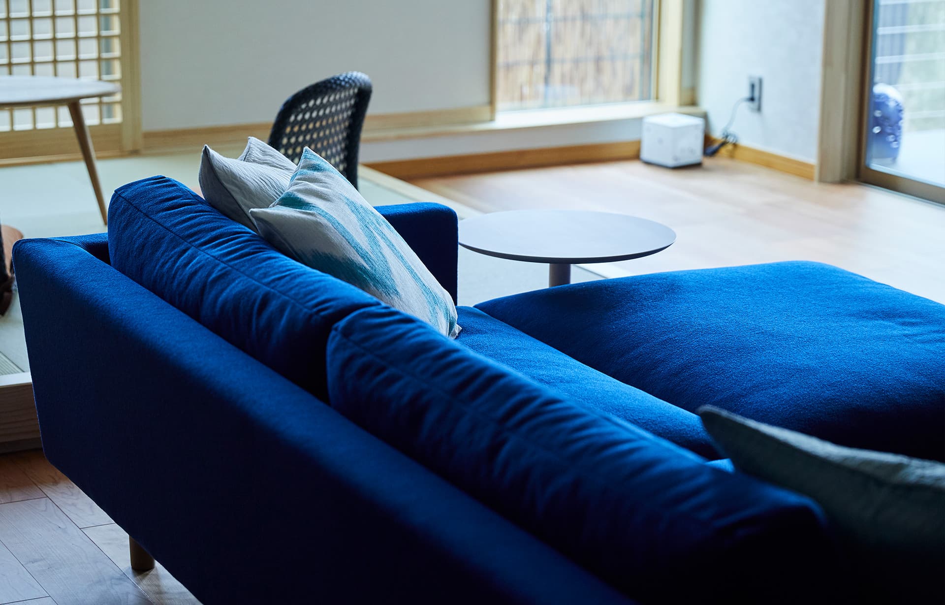 Guest room lounge at IBUKU with a deep blue sofa and tatami corner overlooking a bright wood-floored sitting space