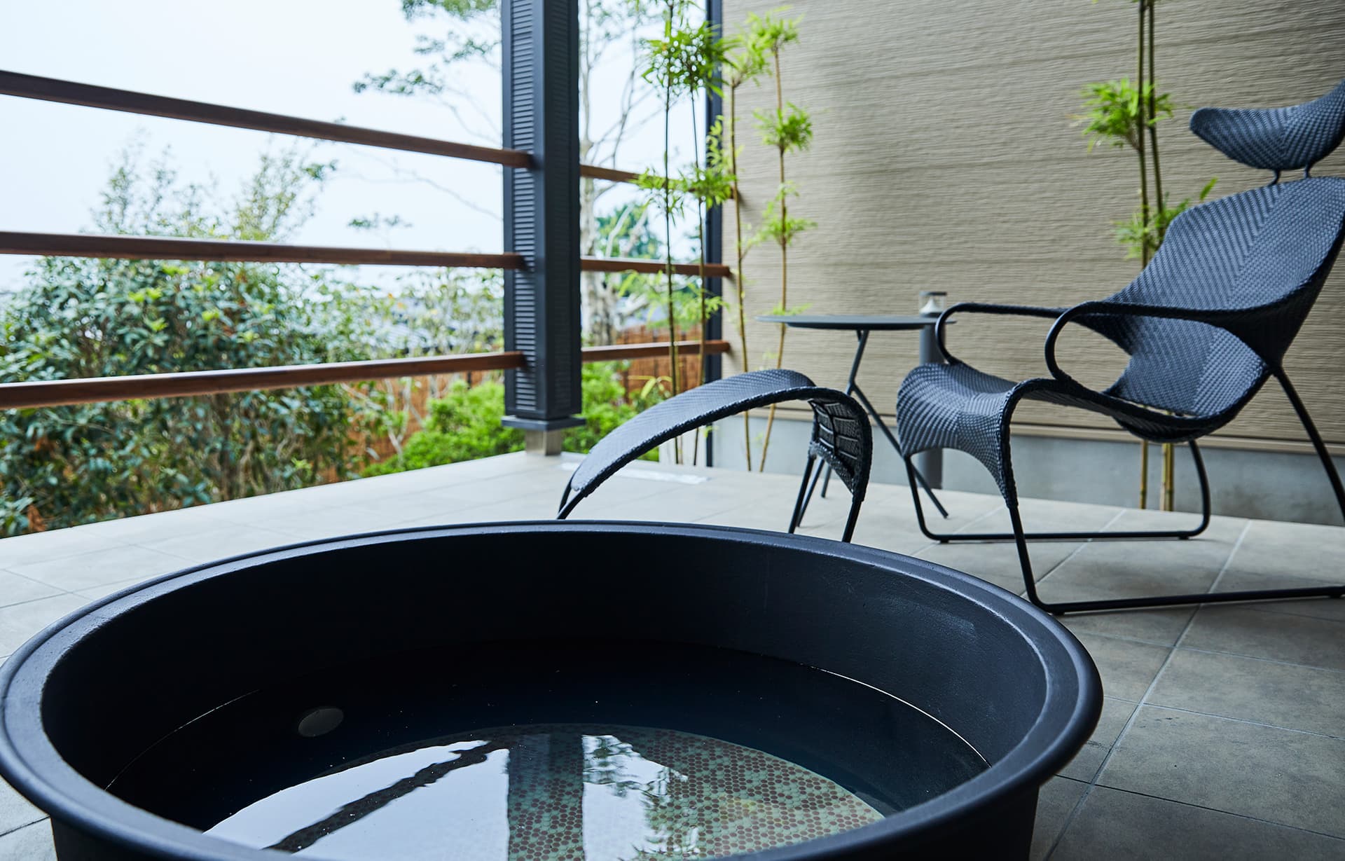 Private round open-air bath on a villa terrace at IBUKU Miyahama Onsen with rattan chairs and bamboo greenery
