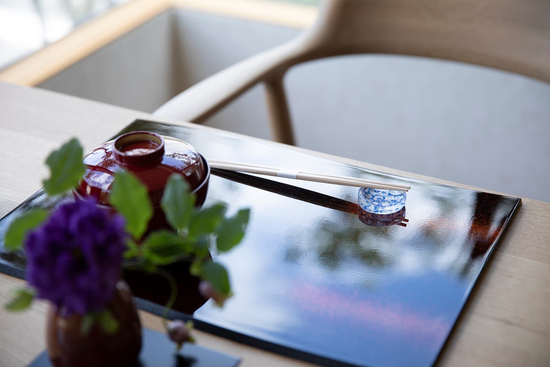 Dining table detail at IBUKU with a black lacquer tray, red lacquered soup bowl, chopsticks and a small flower vase