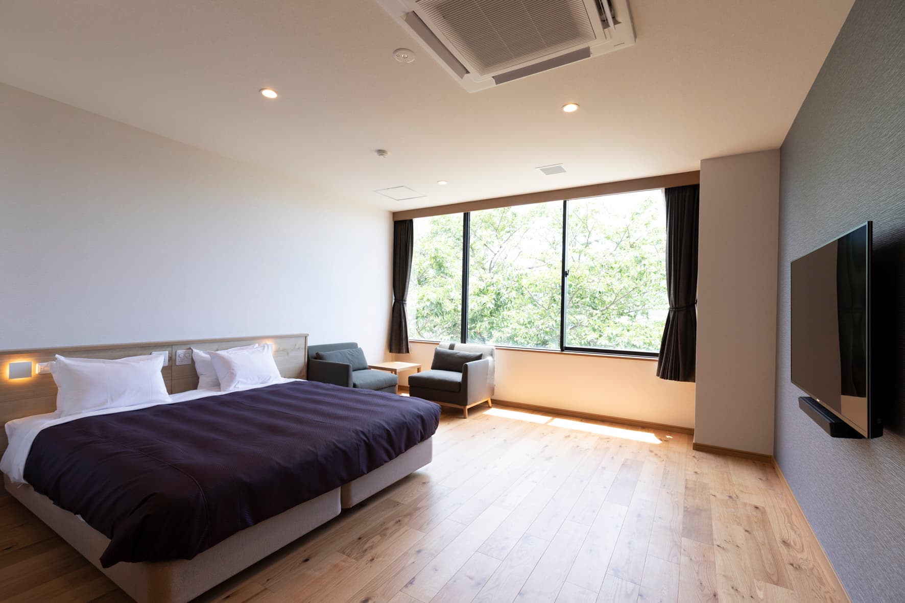 Spacious modern guest room at IBUKU with twin beds, a lounge seating area and large windows framing green treetops