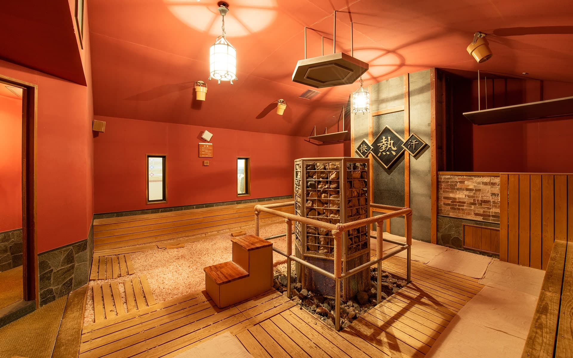 Warm-lit bedrock bath and sand-steam wellness room with wooden flooring and hanging lanterns at Ibusuki Kokoro no Yado