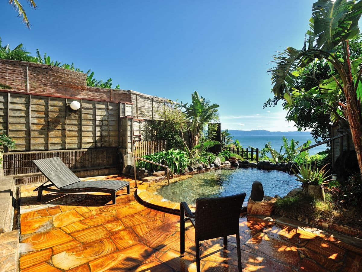 Stone-paved rotenburo terrace with lounge seating overlooking Kinko Bay at Ibusuki Royal Hotel