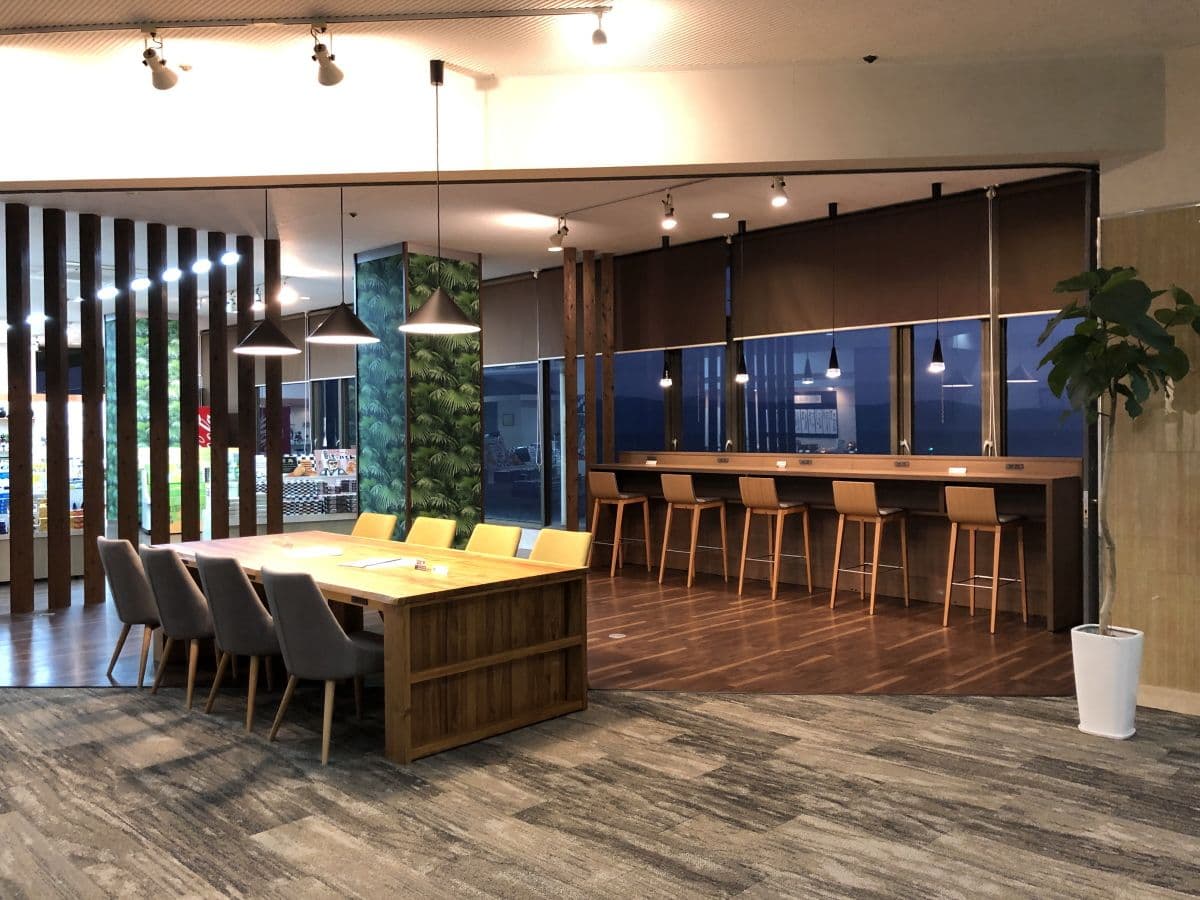 Open dining lounge with communal wood table, counter seating and large windows facing the sea