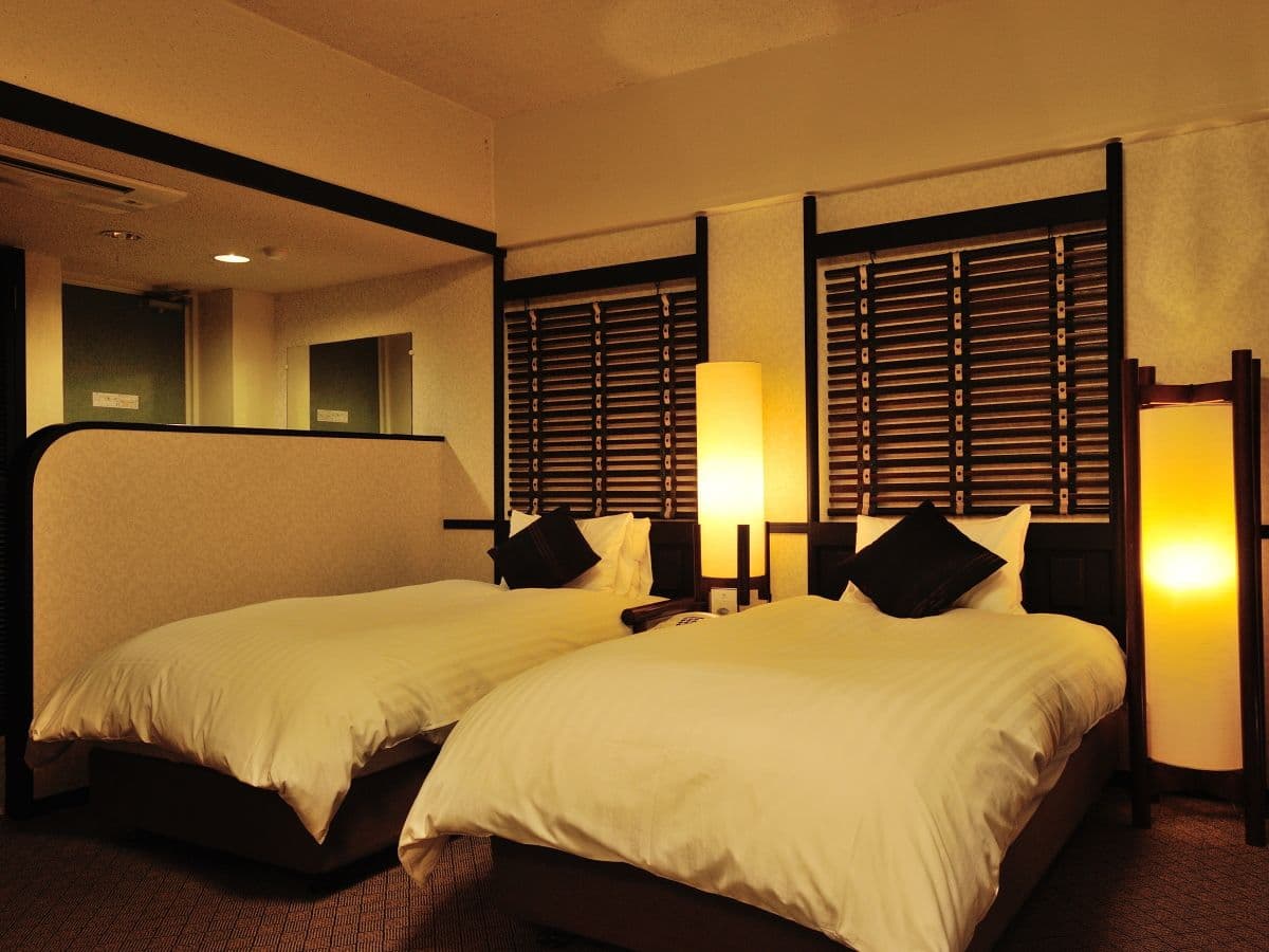 Warmly lit guest room with twin beds, paper lantern lamps and dark wood shutters at Ibusuki Royal Hotel