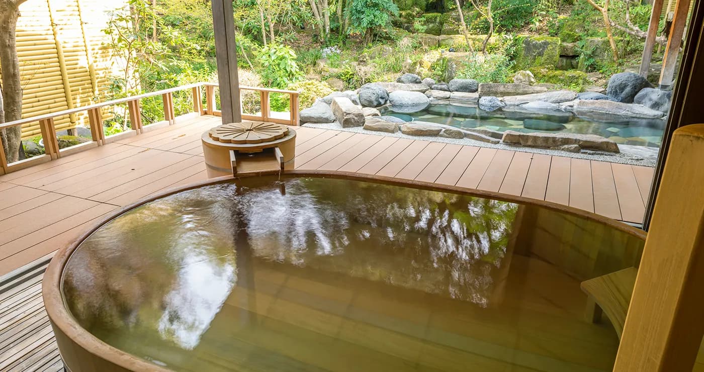 Round wooden hot spring tub on a deck beside an open-air bath at Yu-Kairo Kikuya