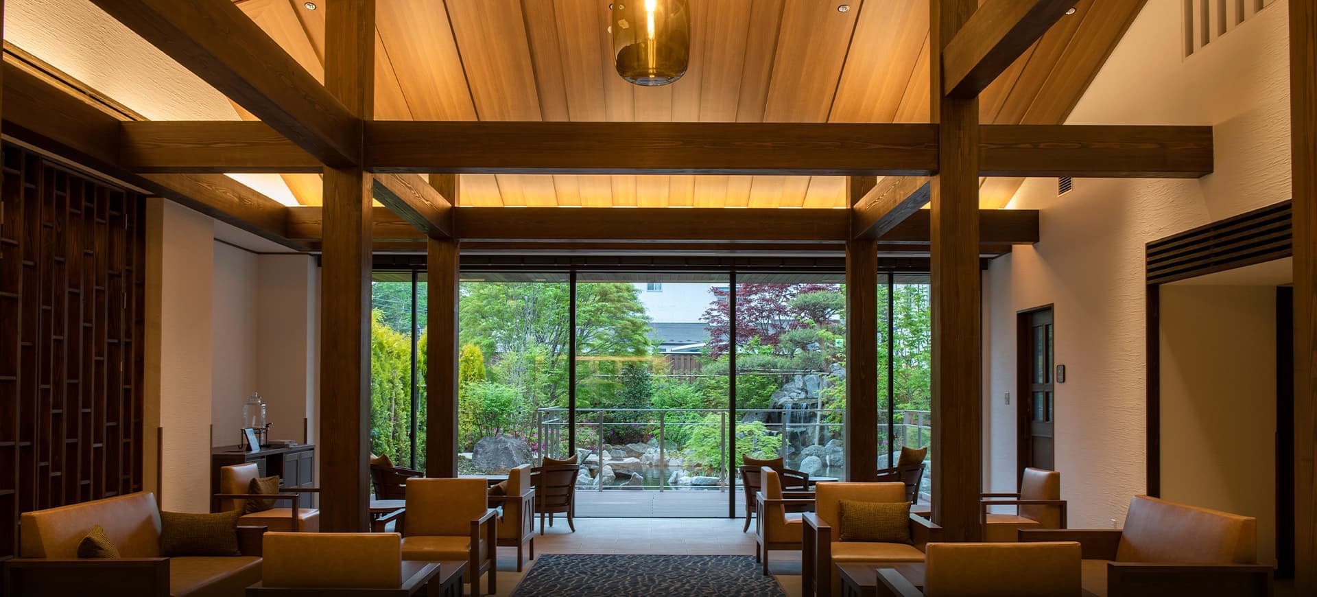 Timber-framed lobby lounge at La Vista Kusatsu Hills with leather armchairs facing a garden through floor-to-ceiling glass