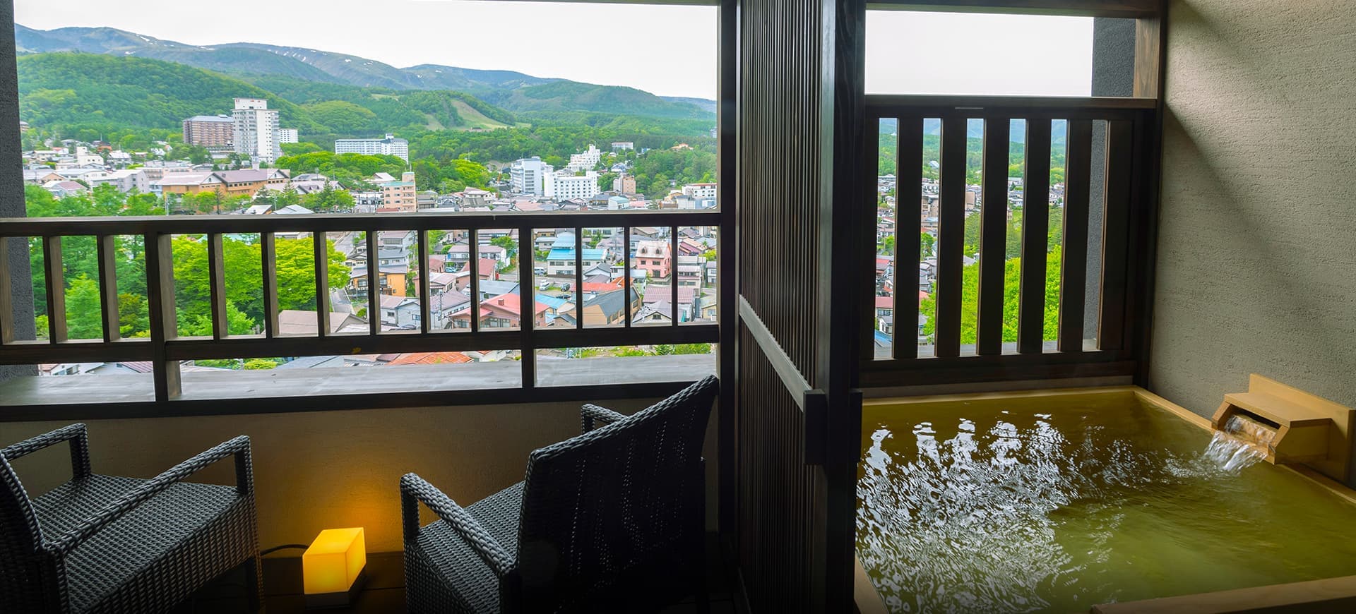 In-room private open-air hot spring bath at La Vista Kusatsu Hills with two chairs and a panoramic view of Kusatsu and the hills