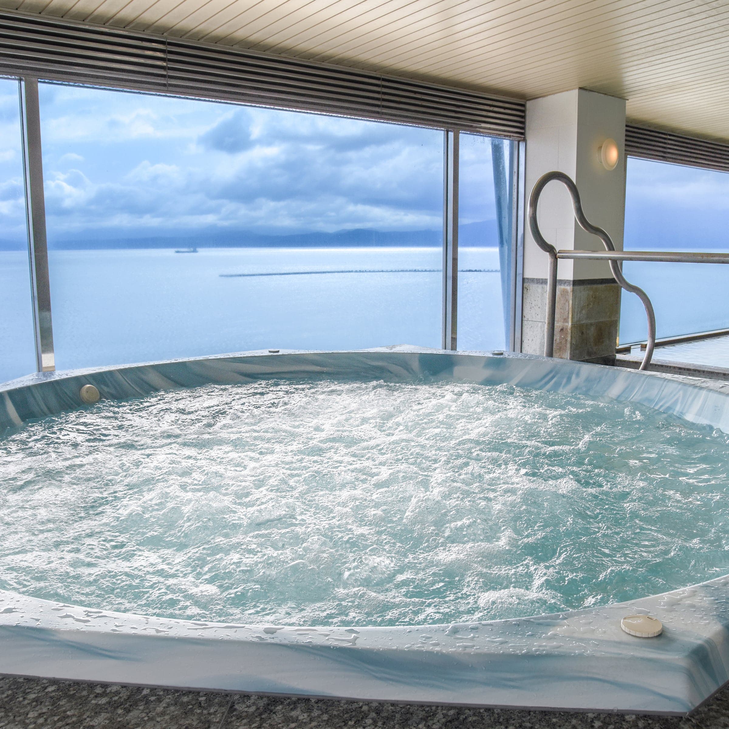 Indoor jacuzzi bath with bubbling water and panoramic sea-view windows at Ibusuki Kaijo Hotel