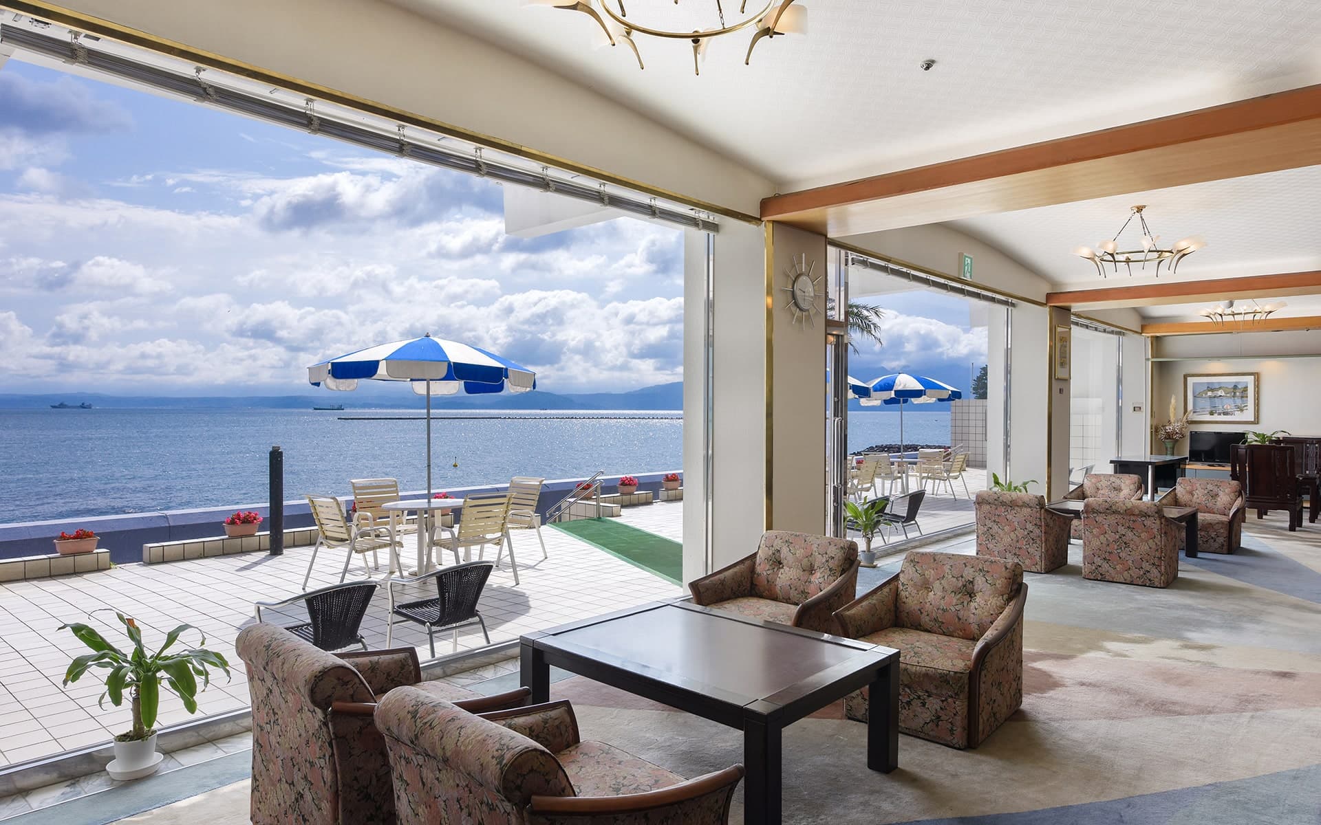 Lobby lounge with armchairs opening onto a sea-view terrace with parasols at Ibusuki Kaijo Hotel