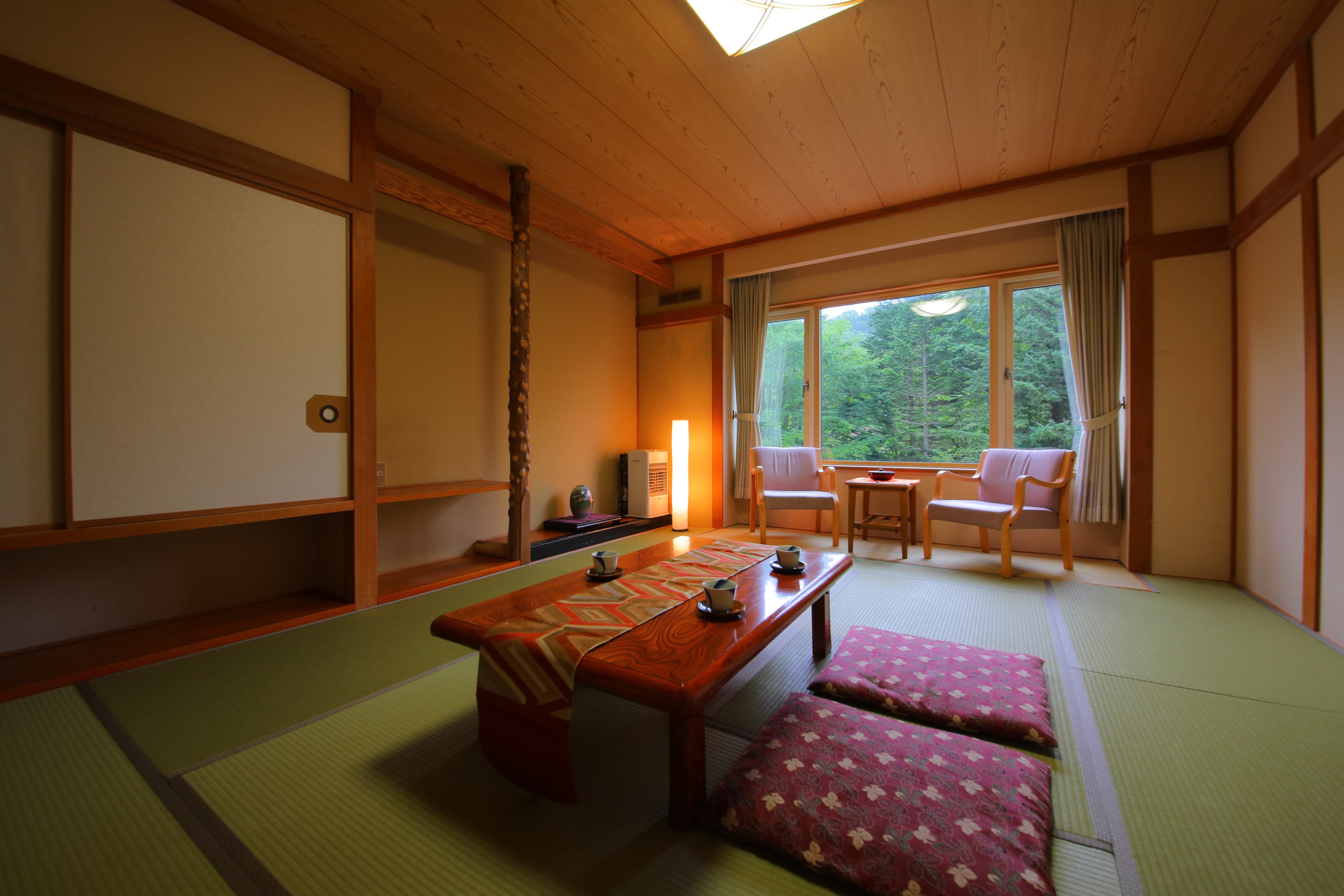 Spacious tatami guest room with a natural-wood pillar, low table and forest view at Mori no Yu Sanseikan