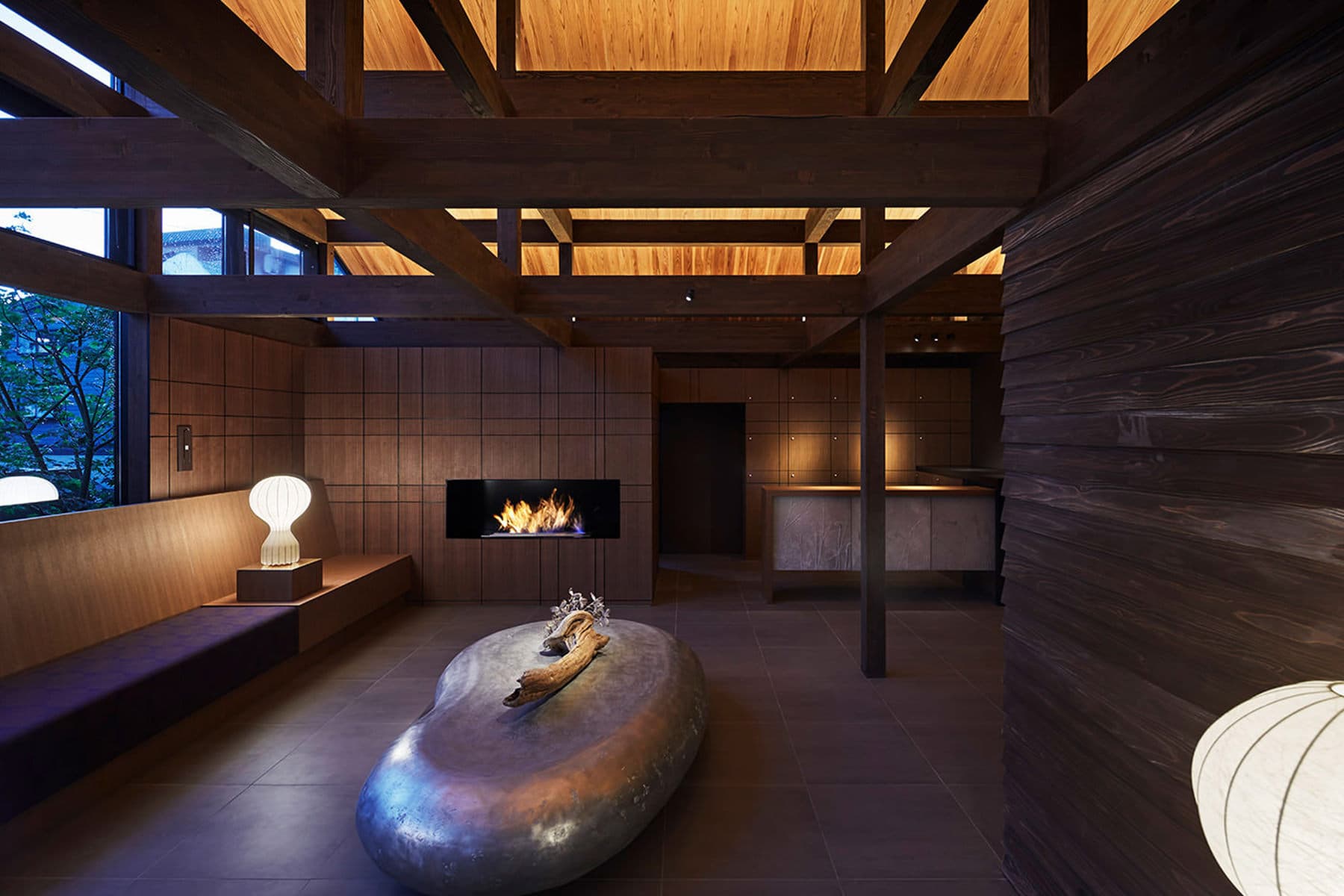 Dark-wood lobby lounge with a modern fireplace, low stone table and timber-beam ceiling