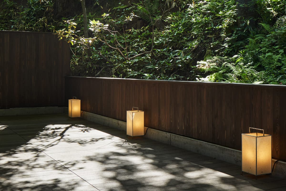 Quiet stone terrace lit by paper lanterns beside lush sunlit greenery