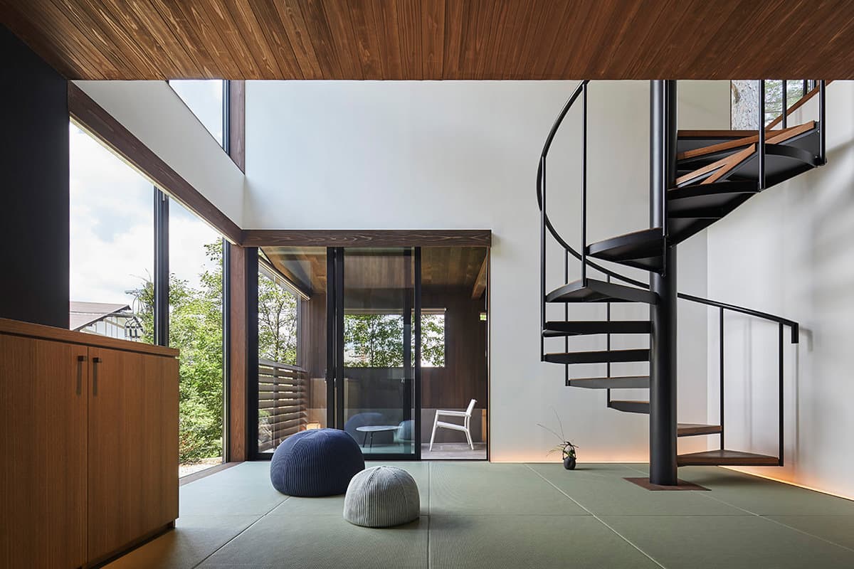 Spacious tatami guest room with a black spiral staircase and floor-to-ceiling garden windows