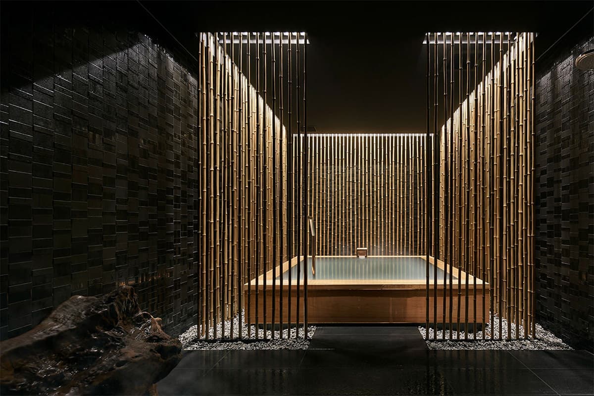 Moody indoor hot-spring bath framed by vertical bamboo screens and dark tiled walls