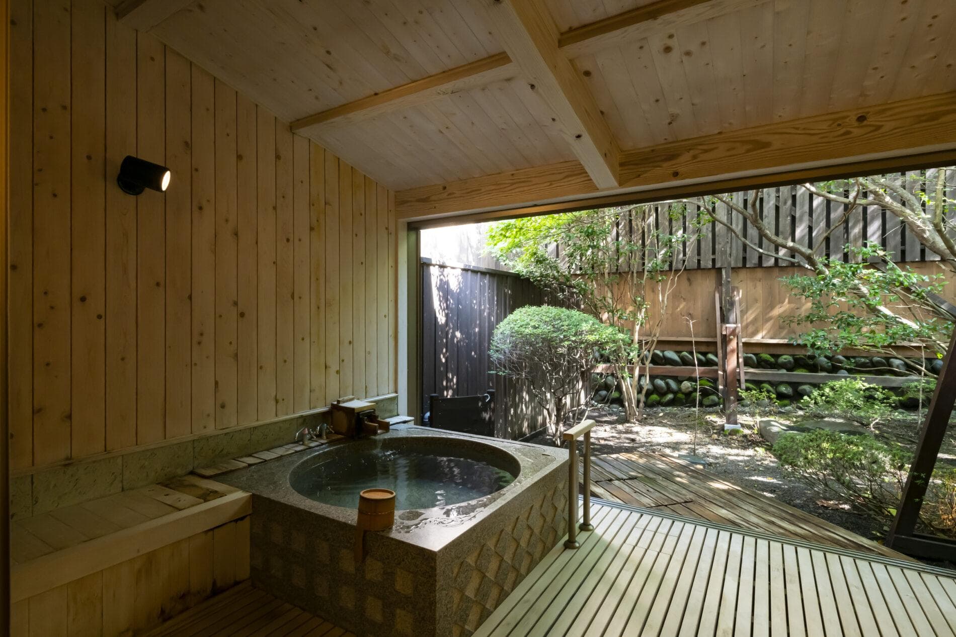 Private open-air bath with wooden surrounds facing a garden