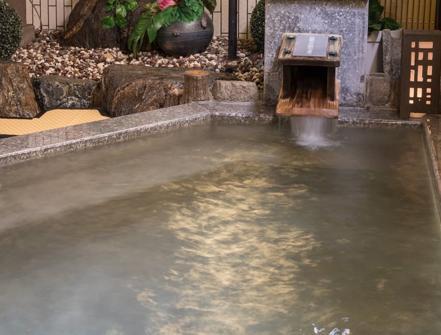 Outdoor rotenburo hot spring at Kiyonoya with steaming mineral water flowing from a wooden spout beside a stone garden