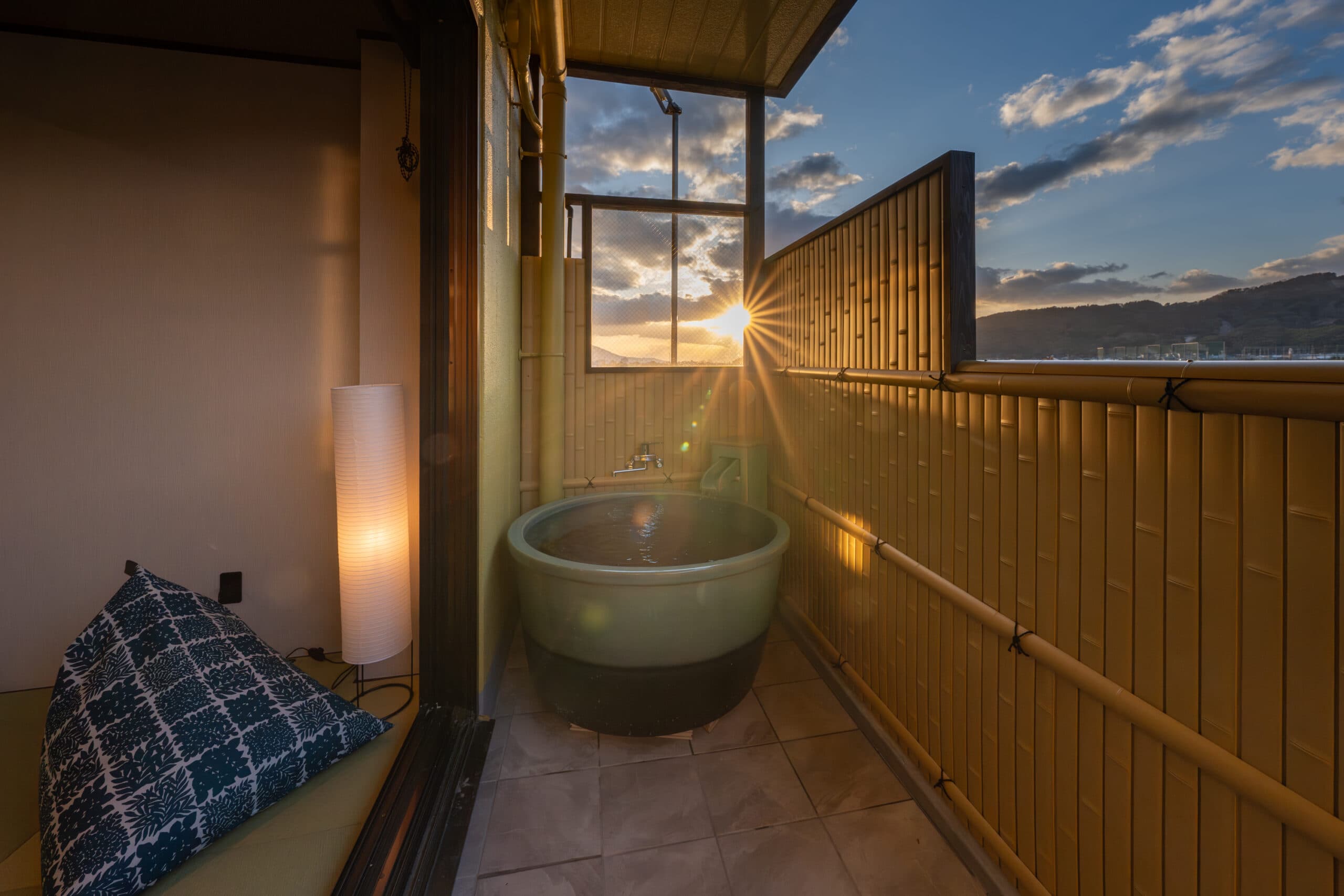 Private open-air ceramic bath on a guest-room balcony at Kiyonoya glowing at sunset behind a bamboo screen