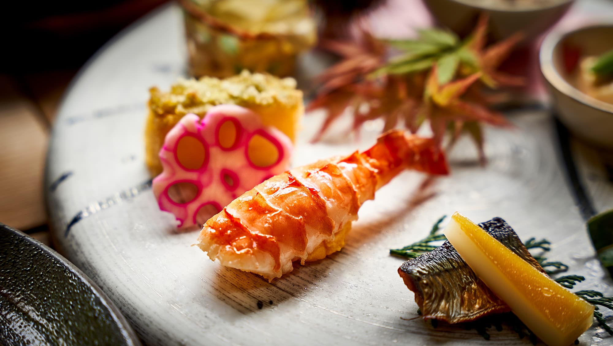 Plated kaiseki course with grilled prawn, lotus root and autumn-leaf garnish at Koto no Niwa