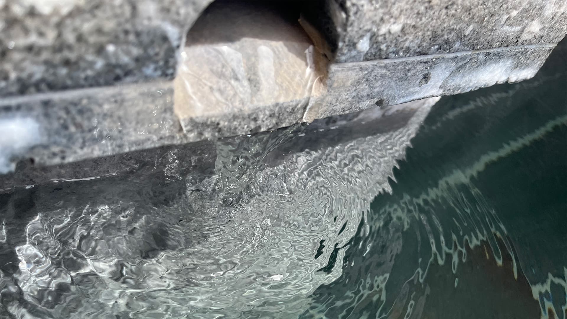 Close-up of natural hot spring water flowing from a wooden spout into the bath at Vent Vert