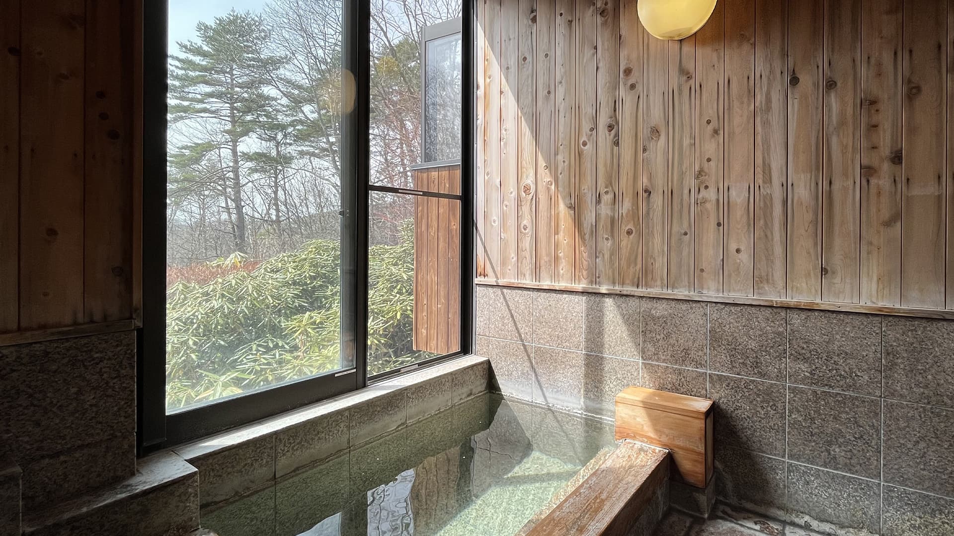 Private reserved onsen bath with green source water beside a forest-view window and cedar panelling at Vent Vert