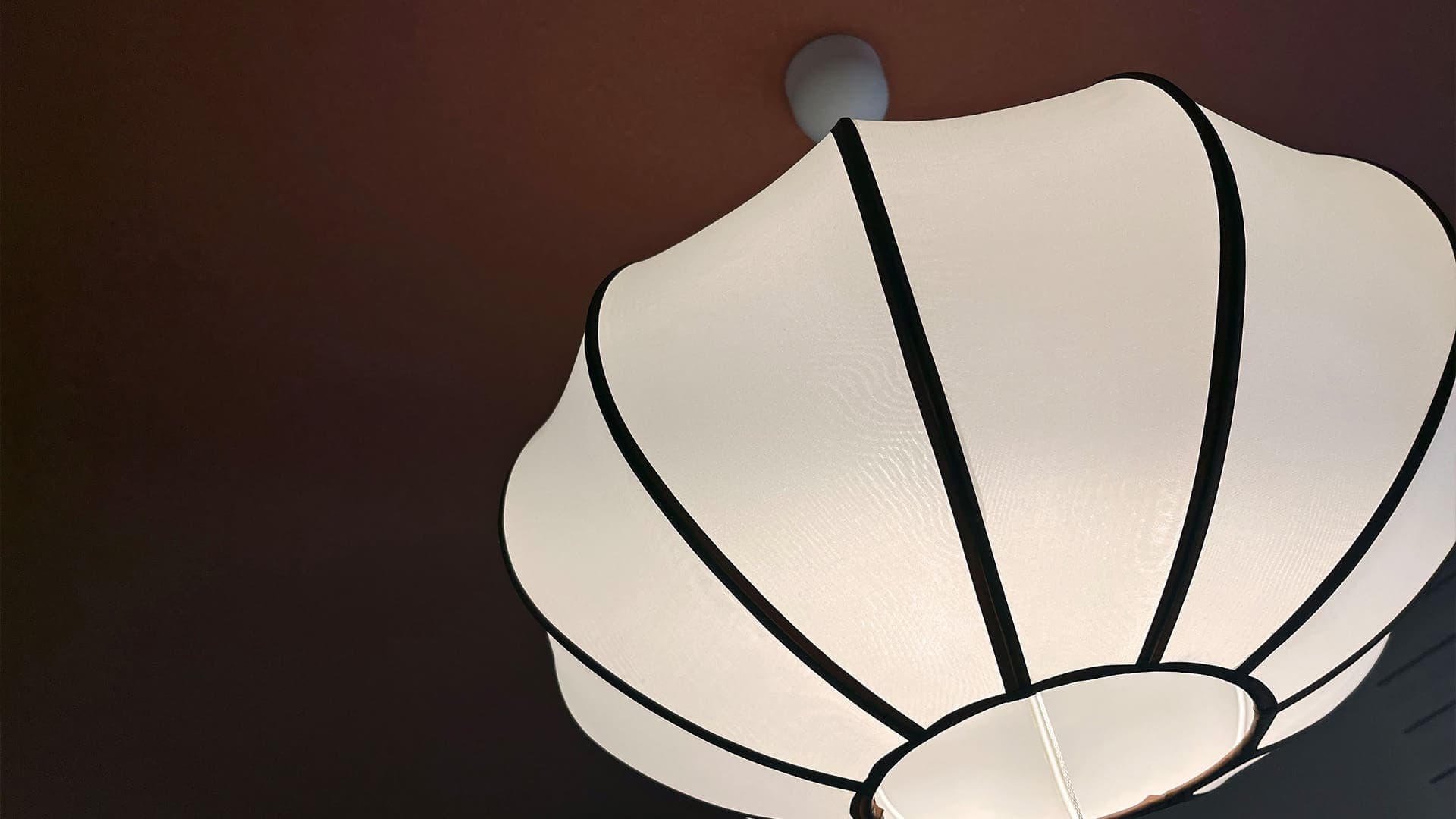Elegant white fabric pendant lamp against a deep wall interior detail at Vent Vert