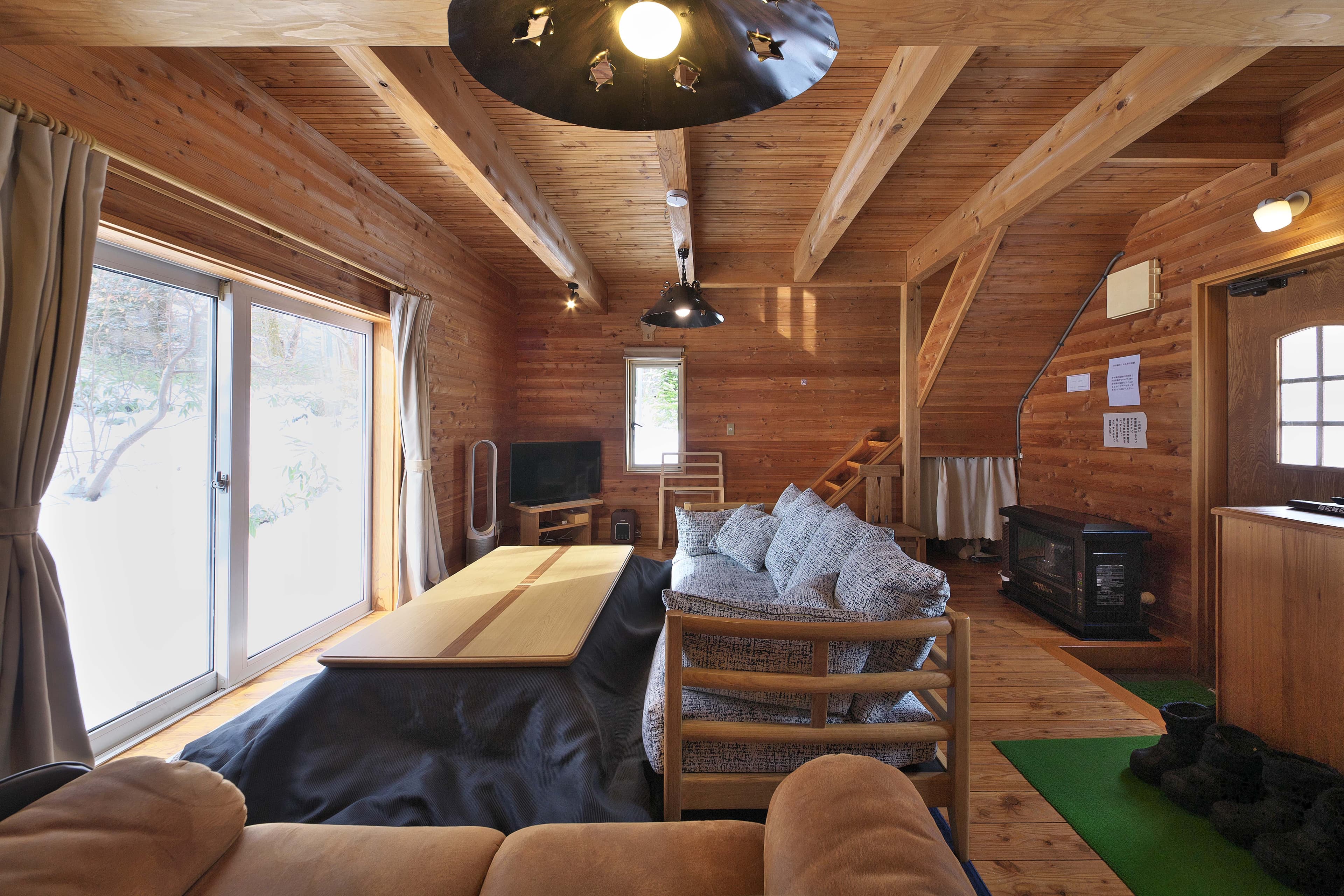Log-cabin cottage interior with timber walls, a wood stove and a lofted ceiling with sofa seating