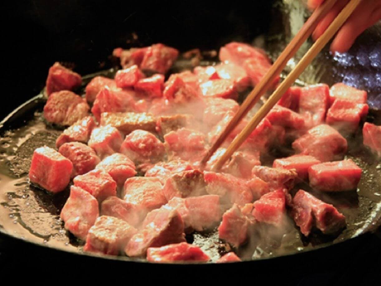 Cubes of marbled wagyu beef searing on a hot teppan griddle at Park Hotel Miyabitei in Noboribetsu Onsen