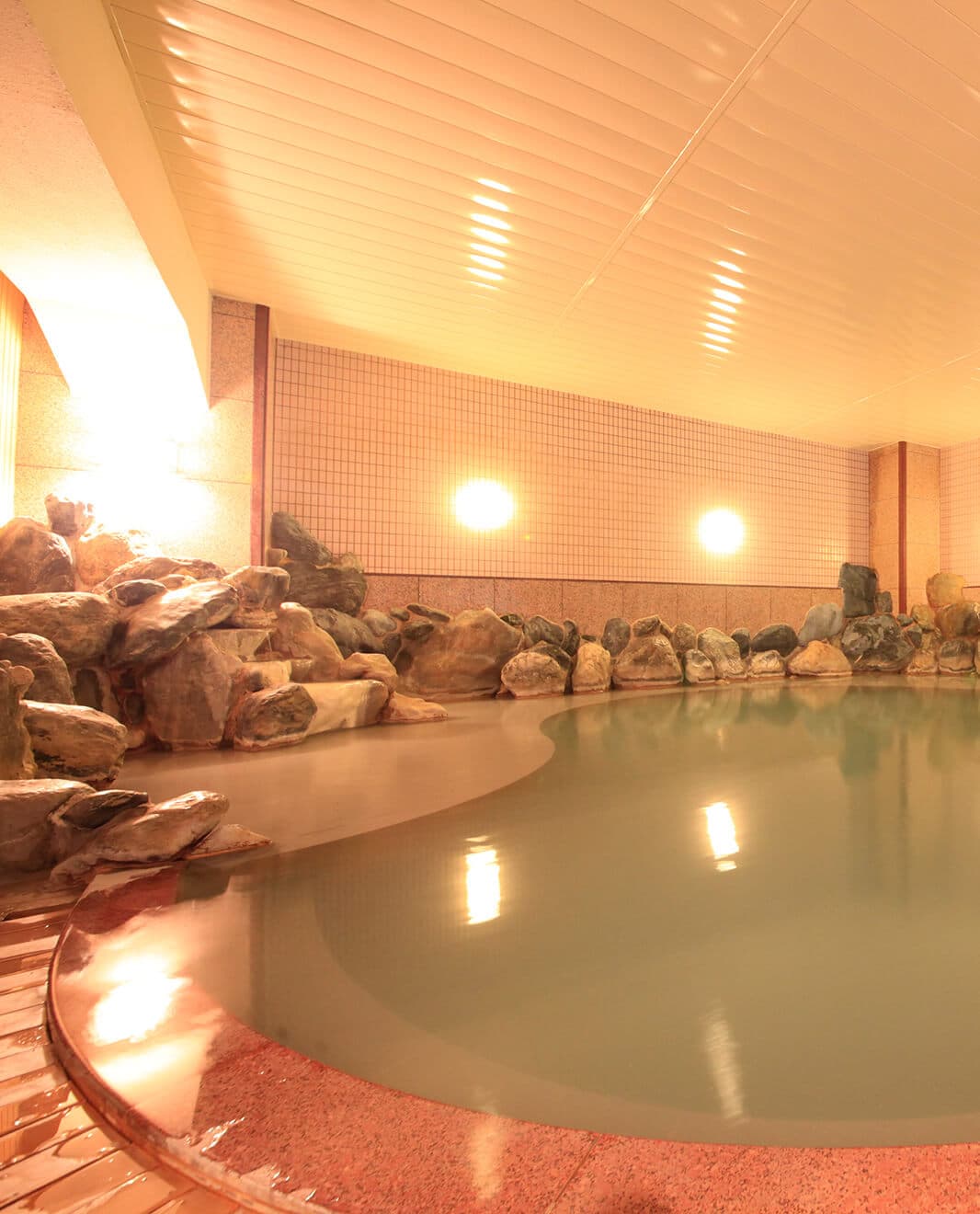 Indoor hot-spring bath edged with boulders and tiled walls glowing under warm lighting at Park Hotel Miyabitei in Noboribetsu Onsen