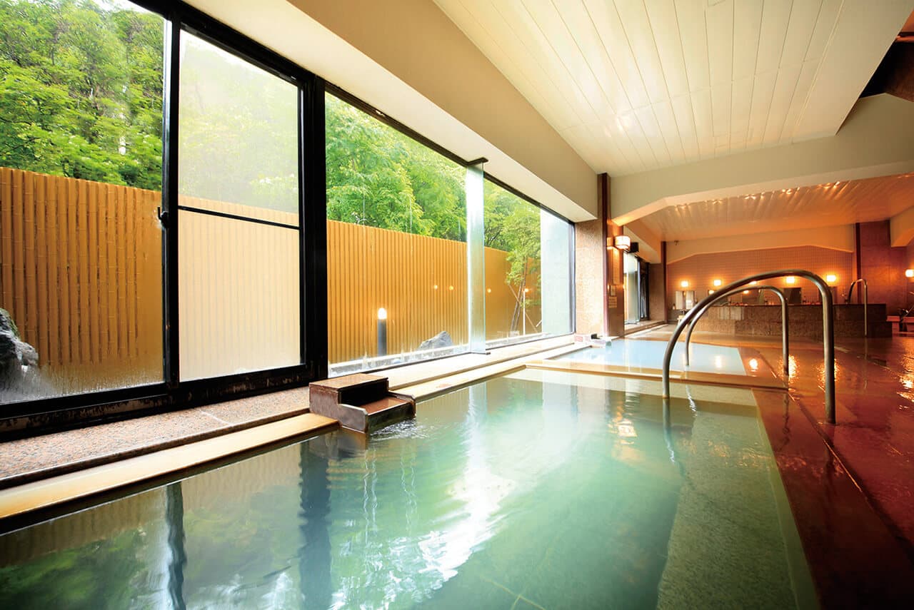 Spacious indoor onsen bath with large windows opening onto greenery at Park Hotel Miyabitei in Noboribetsu Onsen