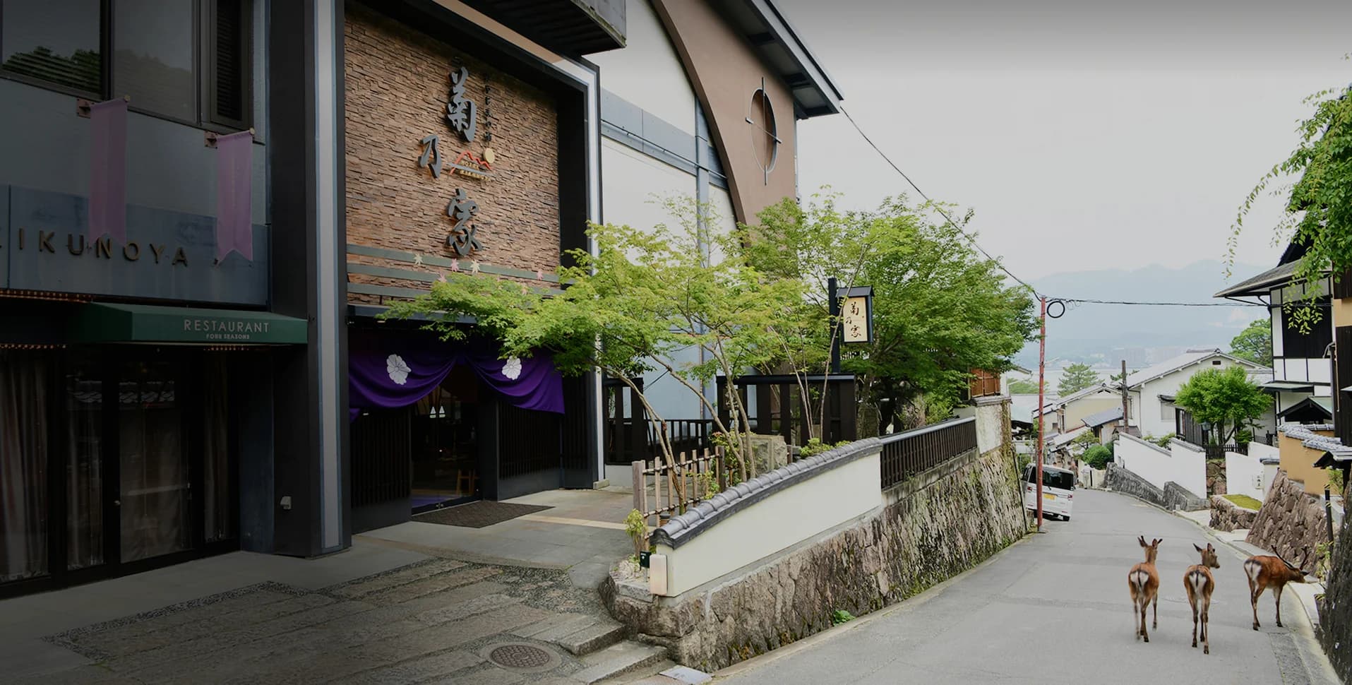 Hotel Kikunoya exterior on Miyajima island with wild deer on the hillside lane and traditional dark-timber facade