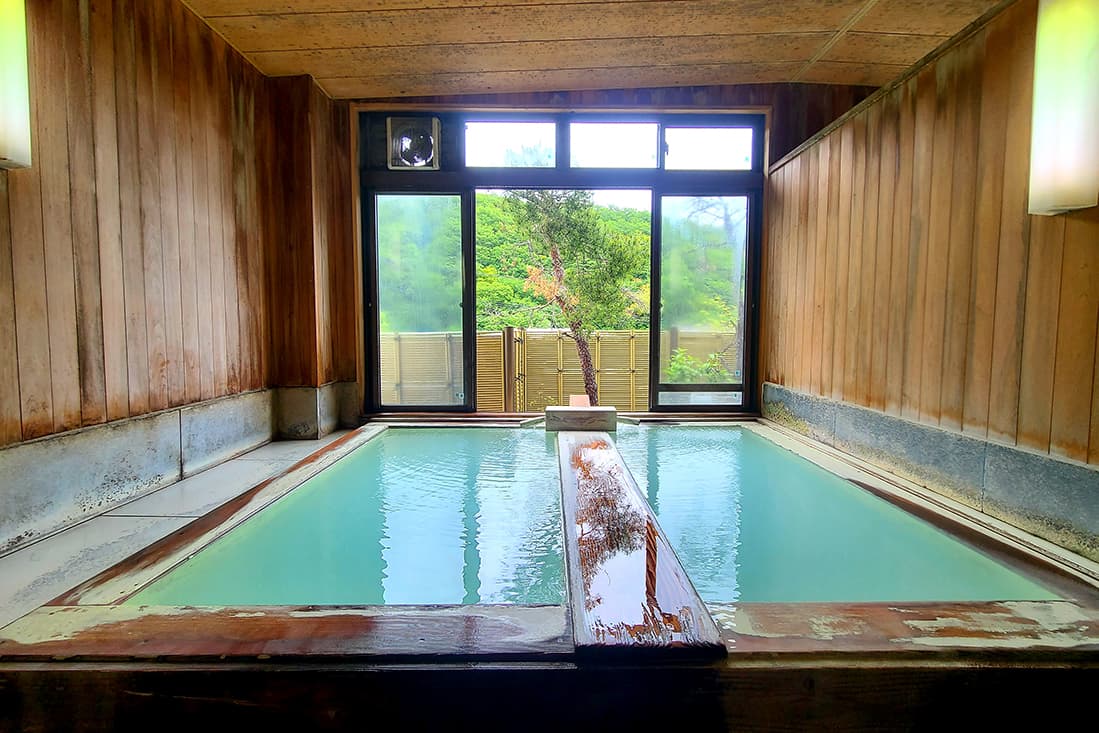 White sulfur hot spring bath in a cypress-panelled room overlooking greenery